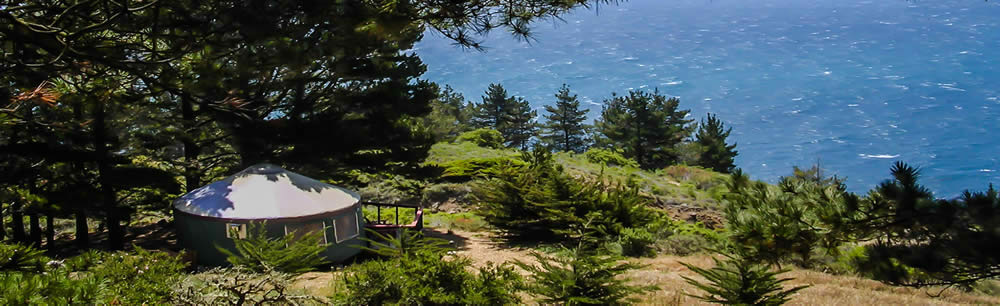 A yurt surrounded by nature with the ocean in view.